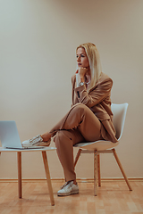 Image showing A professional businesswoman sits on a chair, surrounded by a serene beige background, diligently working on her laptop, showcasing dedication and focus in her pursuit of success