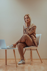 Image showing A professional businesswoman sits on a chair, surrounded by a serene beige background, diligently working on her laptop, showcasing dedication and focus in her pursuit of success