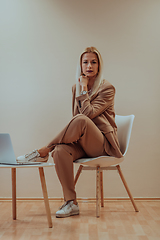 Image showing A professional businesswoman sits on a chair, surrounded by a serene beige background, diligently working on her laptop, showcasing dedication and focus in her pursuit of success