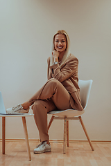 Image showing A professional businesswoman sits on a chair, surrounded by a serene beige background, diligently working on her laptop, showcasing dedication and focus in her pursuit of success