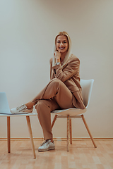 Image showing A professional businesswoman sits on a chair, surrounded by a serene beige background, diligently working on her laptop, showcasing dedication and focus in her pursuit of success