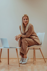 Image showing A professional businesswoman sits on a chair, surrounded by a serene beige background, diligently working on her laptop, showcasing dedication and focus in her pursuit of success