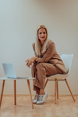 Image showing A professional businesswoman sits on a chair, surrounded by a serene beige background, diligently working on her laptop, showcasing dedication and focus in her pursuit of success