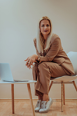 Image showing A professional businesswoman sits on a chair, surrounded by a serene beige background, diligently working on her laptop, showcasing dedication and focus in her pursuit of success