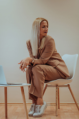 Image showing A professional businesswoman sits on a chair, surrounded by a serene beige background, diligently working on her laptop, showcasing dedication and focus in her pursuit of success