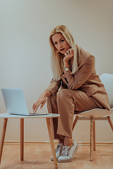 Image showing A professional businesswoman sits on a chair, surrounded by a serene beige background, diligently working on her laptop, showcasing dedication and focus in her pursuit of success