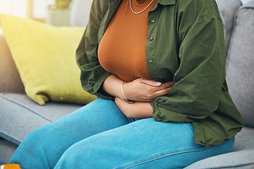 Image showing Hands, stomach and menstruation with a woman in pain on a sofa in the living room of her home closeup. Pregnant, gas or indigestion with a female holding her belly for a medical or colon problem