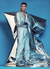 Image showing Fashion, cyberpunk and silver with a man on a blue background at a photo shoot in a shiny futuristic outfit. Sci fi, creative or art with a young model in studio for holographic or vaporwave clothes