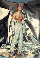 Image showing Portrait, cyberpunk and silver with a trendy man at a photo shoot in a shiny outfit for futuristic style. Fashion, sci fi or creative with a young model in studio for holographic or vaporwave clothes