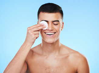 Image showing Skincare, beauty and man with cotton pad in a studio for health, wellness and self care routine. Smile, dermatology and young male model cleaning with facial cosmetic swab product on blue background