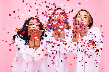 Image showing Blow, friends and women in studio with confetti for clothing promotion, fashion sale and discount. Excited, diversity and female people on pink background for bonding, celebration and having fun