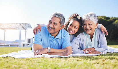 Image showing Grandparents, girl and blanket on grass, relax and smile with hug, love and picnic on family vacation in summer. Senior man, woman and grandchild with embrace, thinking and happy in sunshine on lawn