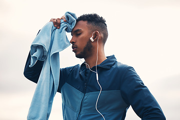 Image showing Tired runner man, outdoor and towel with earphones, music and cleaning for sweat, hygiene and wellness in morning. Guy, thinking and training for marathon with fatigue, cloth and burnout in nature