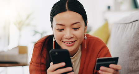 Image showing Asian woman, credit card and phone relaxing on her sofa online shopping, ecommerce and fintech easy payment. Young person in China typing bank information on cellphone for finance transaction at home