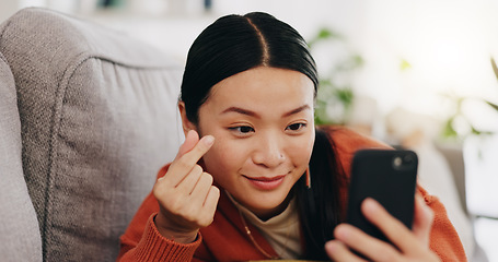 Image showing Asian woman, selfie and lying on sofa with heart sign and love for profile picture, vlog or social media at home. Happy female relaxing with smile and hand signs for photo or online vlogging on couch