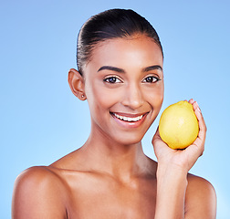 Image showing Lemon, portrait and beauty of happy woman in studio for vitamin c benefits, eco cosmetics or nutrition. Face of indian model, healthy skincare and citrus fruit of vegan dermatology on blue background
