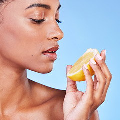 Image showing Woman, face and lemon in studio for beauty, vitamin c cosmetics and natural nutrition. Indian model, healthy skincare and eating citrus fruits for vegan dermatology, mockup space and blue background