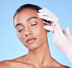 Image showing Needle, woman and face in studio for skincare, beauty process and aesthetic filler on blue background. Indian model, hands of surgeon and injection for plastic surgery, facial change or prp cosmetics