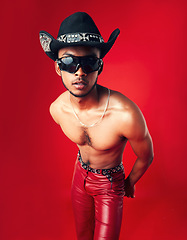 Image showing Fashion, man and cowboy in hat, shirtless with sunglasses and gen z isolated on red background. Confident model, cool and leather pants with eyewear accessory, western aesthetic and edgy in studio