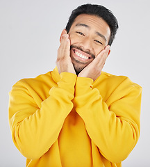 Image showing Smile, shy and hands on face of asian man in studio for in love, sweet or gesture on grey background. Happy, portrait and Japanese male model pose with emoji cheeks expression for romantic sign