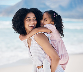 Image showing Happy, piggyback and mother with child at the beach on a family vacation, adventure or holiday. Smile, love and young mom carrying, playing and bonding with her girl kid by the ocean on weekend trip.