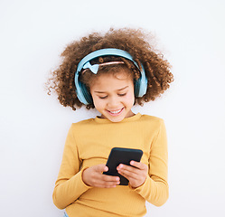 Image showing Girl kid, chat and smartphone, headphones and music with smile isolated on white background. Technology, audio streaming and social media, using phone and child with mobile app and radio in studio