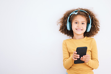 Image showing Girl kid, portrait and smartphone, headphones and music with smile isolated on white background. Technology, audio streaming and social media, mockup space and child, mobile app and radio in studio