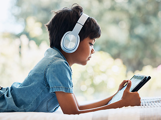 Image showing Boy child, tablet and headphones on bed, reading or idea with e learninng, movie and web video to relax. Male child, digital touchscreen and thinking in bedroom for games, music and streaming in home