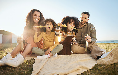 Image showing Parents, children and fun bubbles at picnic at beach vacation home with smile, love and relax. Mom, dad and kids on blanket on grass with soap bubble wand, bonding ocean holiday together in summer.