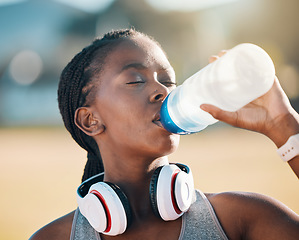 Image showing Black woman, drinking water and health, fitness and runner outdoor with headphones, thirsty after workout with cardio. Bottle, hydration and h2o, exercise and wellness with athlete, music and sports