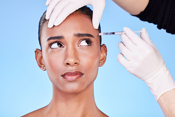 Image showing Injection, hands and face of Indian woman for plastic surgery, cosmetics and skincare in studio. Dermatology needle, anxiety and surgeon and person for anti aging, botox and beauty on blue background