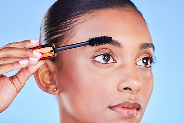 Image showing Woman, face and mascara in beauty makeup, cosmetics or eye brush against a blue studio background. Closeup of female person applying eyeshadow on eyelashes for volume, product or facial treatment