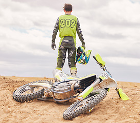 Image showing Bike. sand and the back of a sports man outdoor on a dirt track after an accident or fall during a race. Motorcycle, freedom and challenge with a male athlete against a gray sky in the desert