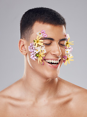 Image showing Smile, skincare and a man with flowers on a studio background for creative aesthetic. Happy, plant and a male model with floral art for facial wellness and dermatology isolated on a studio backdrop