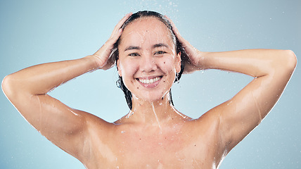 Image showing Face, shower and woman smile washing hair in studio isolated on blue background. Water splash, hygiene and portrait of natural Asian model happy, cleaning or bathing for wellness, beauty and cosmetic