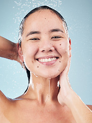 Image showing Skincare, water splash and face of woman cleaning in studio isolated on a blue background. Shower, hygiene and portrait of happy Asian model washing, cosmetic and bath for wellness, health and beauty
