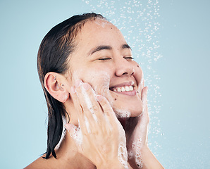 Image showing Skincare, shower soap and happy woman cleaning in studio isolated on a blue background. Water splash, hygiene foam and model smile, washing and bathing in wellness, healthy skin or beauty in bathroom