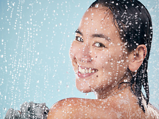 Image showing Portrait, woman and shower with water, soap and sponge for cleaning with dermatology, skincare and blue background in studio. Person, smile and washing skin and body with foam bubbles in bathroom