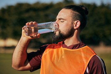 Image showing Sports, drinking water and man in field to rest after training, workout and exercise outdoors. Fitness, health and male athlete with liquid bottle for wellness, nutrition and hydration for practice