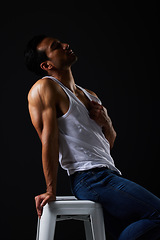 Image showing Sexy, muscle and man on chair on black background with fitness inspiration, beauty aesthetic and sensual fashion. Erotic art, sexual body and male model sitting in studio, thinking in dark lighting.