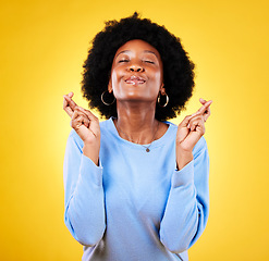 Image showing Woman, fingers crossed and smile in studio for hope, trust and optimism of competition, prize or lottery. Happy african model wish for luck, bonus promotion and winning giveaway on yellow background