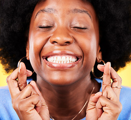 Image showing Black woman, face and fingers crossed in studio for hope, trust and optimism of competition, prize and lottery. Happy model emoji for luck, bonus promotion and winning giveaway on yellow background