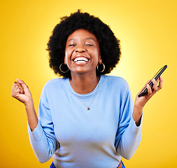 Image showing Woman, phone and fist for success in studio, celebration and winning lottery prize, promotion or bonus on yellow background. Happy african model, mobile app and celebrate online gambling achievement