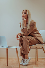 Image showing A professional businesswoman sits on a chair, surrounded by a serene beige background, diligently working on her laptop, showcasing dedication and focus in her pursuit of success