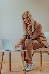 Image showing A professional businesswoman sits on a chair, surrounded by a serene beige background, diligently working on her laptop, showcasing dedication and focus in her pursuit of success