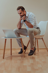 Image showing A confident businessman sitting and using laptop with a determined expression, while a beige background enhances the professional atmosphere, showcasing his productivity and expertise.