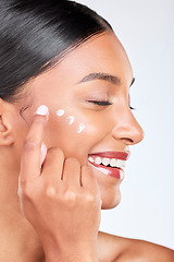 Image showing Smile, skincare and a woman with cream on a white background for beauty, wellness or cosmetics. Happy, collagen and side of an Indian person or model with lotion or sunscreen for a facial treatment