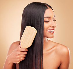 Image showing Hair care, brush and young woman in a studio with salon keratin treatment for wellness and self care. Grooming, cosmetic and Indian female model with tool for hairstyle isolated by a brown background