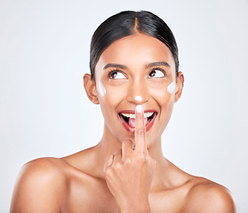 Image showing Cream, woman and facial cosmetics in studio for aesthetic skincare, dermatology or smile on white background. Happy indian model, face lotion and thinking of beauty, sunscreen and healthy moisturizer
