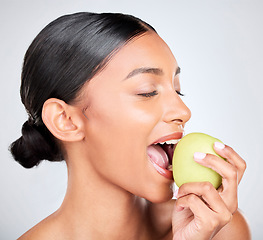 Image showing Face, beauty and woman biting an apple for health, wellness or nutrition in studio on white background. Food, skincare and diet with a young model eating organic green fruit for benefits or digestion